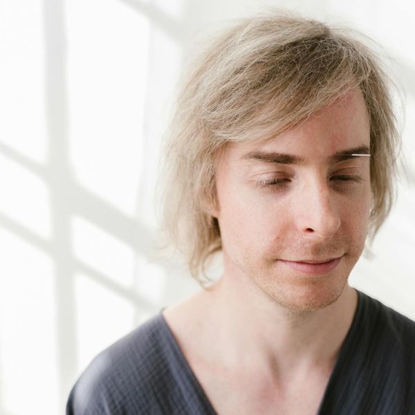 Man smiling with eyes closed in a bright minimalist room.